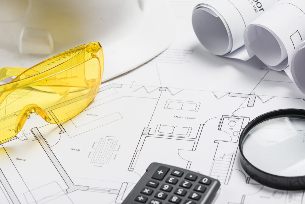 Architekturplan mit Schutzbrille, Lupe, Taschenrechner.